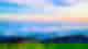 Sunrise at the top of a mountain peak overlooking misty jade green valleys with pale clouds and a rosey blue sky