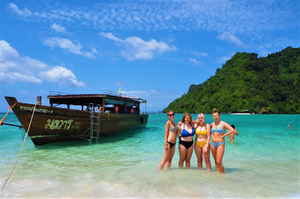 Travellers posing next to traditional thai boat on beach