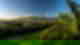 Tropical palm trees with rich green hills and town in the background with volcanoes on blue slightly cloudy day