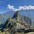 Ancient stone walls woven into green hill overlooking lush mountains on a blue sky day
