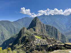 Ancient stone walls woven into green hill overlooking lush mountains on a blue sky day