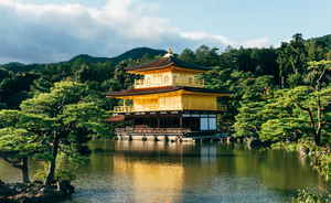 Floating golden traditional temple on pond surrounded by dark forest on a cloudy day