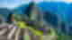 Maze of ancient stone ruins on emerald hills with towering green mountains and blue skies