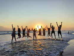 Travellers jumping on balinese beach with sunset behind them