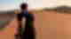 Person in black clothing carrying a sled and walking over golden dunes in the desert at sunset, Huacachina