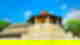Sacred temple with pale yellow architecture and a red and grey-green rooftop on a blue sky day with some clouds