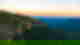Rugged cliffs leading into hills covered in dense dark forest under a sunset sky, The Blue Mountains