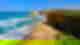 Gold sand with bright blue waves lapping at the shore, mossy brown cliffs and rock stacks in the ocean