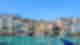 Bright sapphire waters facing out to pastel coloured buildings with blue boats docked in the water under clear blue skies