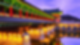Illuminated traditional bridge with bright red columns and emerald details with pagoda rooftops under violet sky and waters
